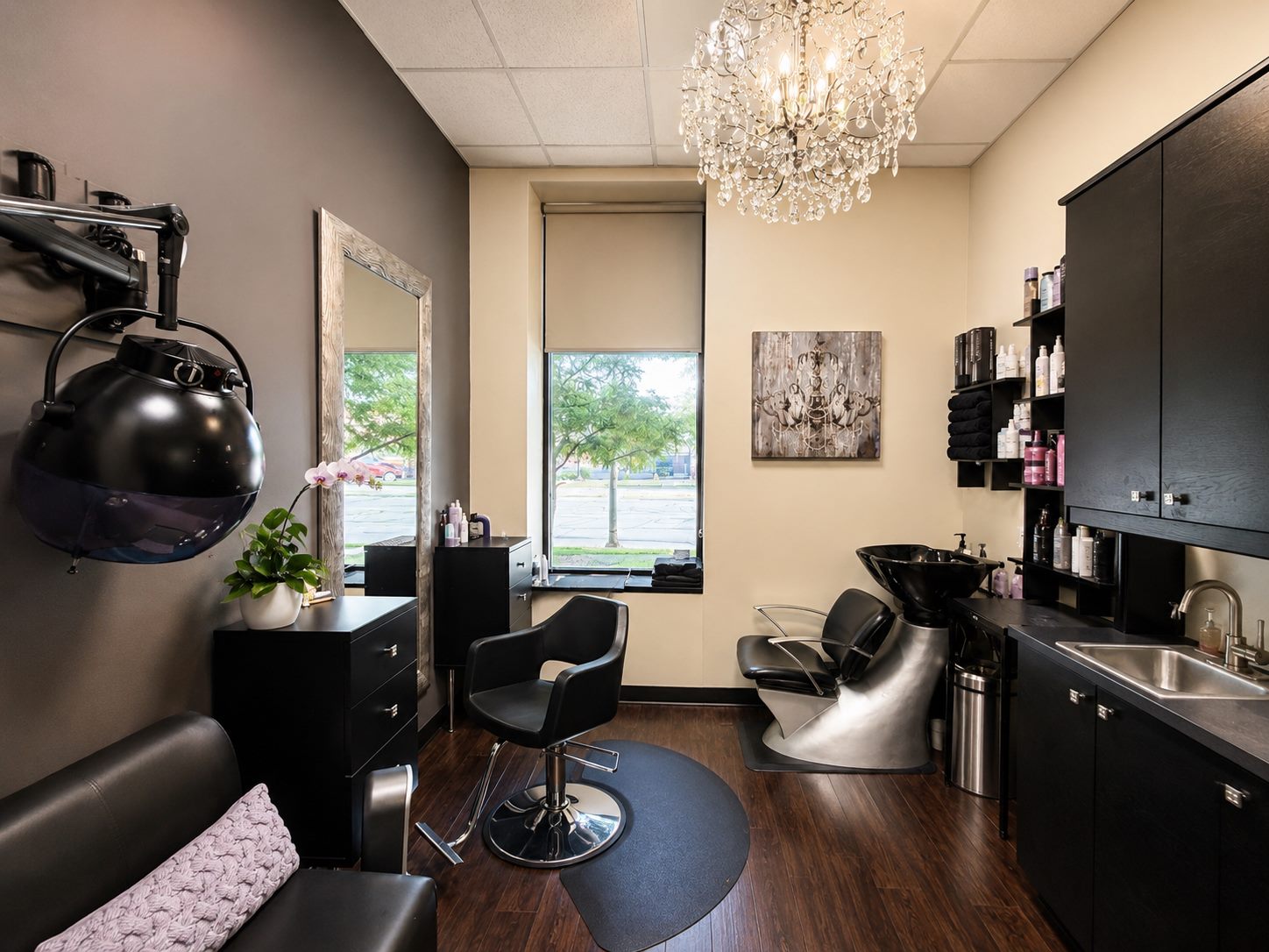 The interior of Liana Hair Studio: a styling chair and mirror, shampoo bowl, and a crystal chandelier.